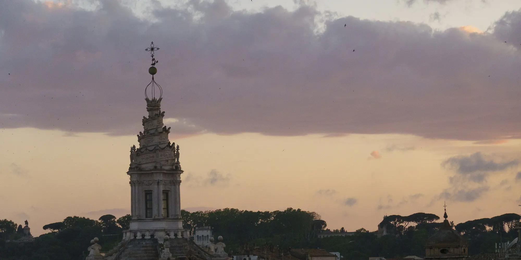 The spiral lantern of Sant'Ivo alla Sapienza above Rome's rooftops in the pink and amber light of evening.